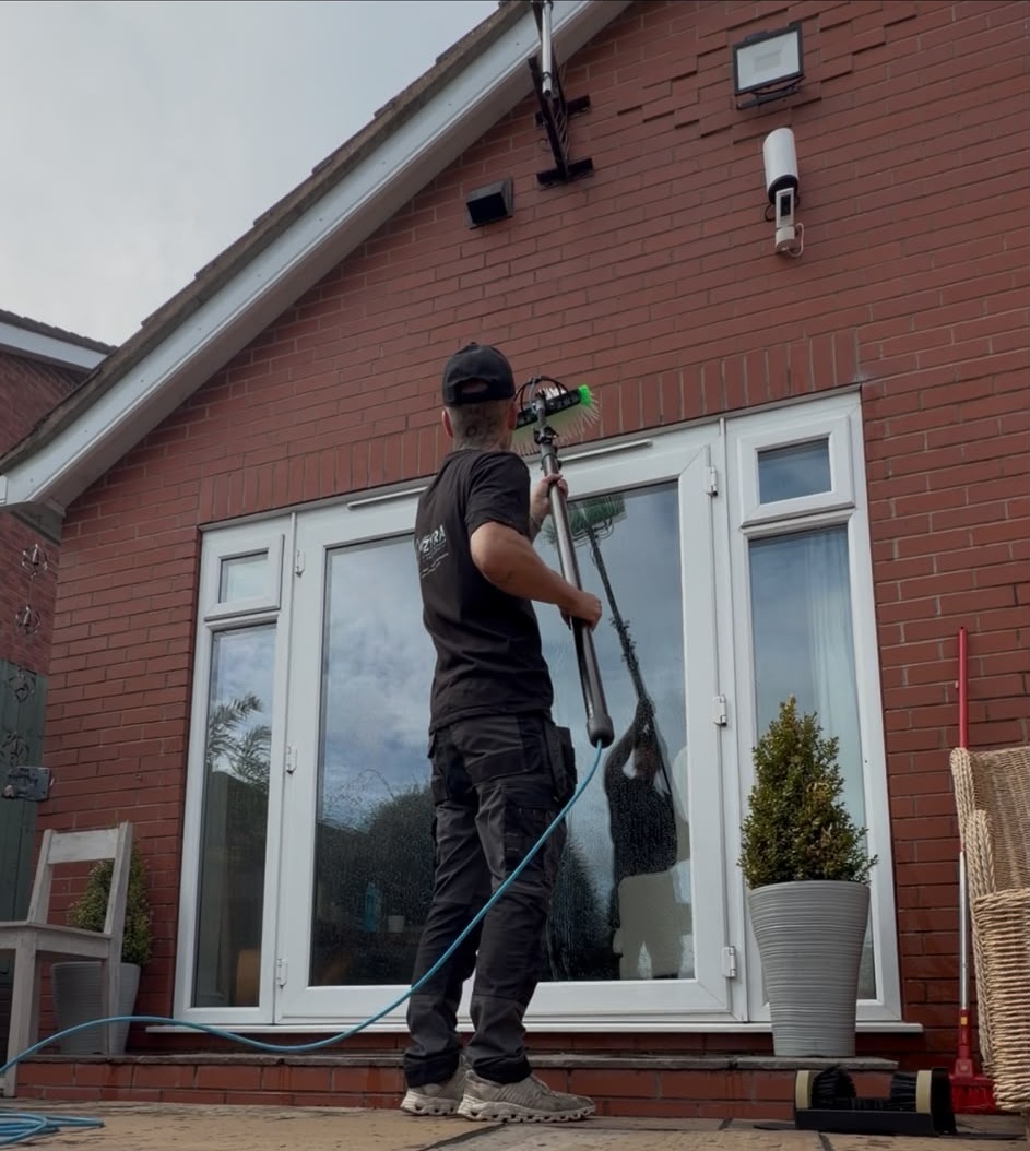 Operator using a water-fed brush pole on the windows and brickwork of a house